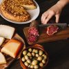 crop-hand-slicing-smoked-meat-near-assorted-food